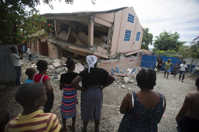 Residents stand looking at a collapsed school damaged by a magnitude 5.9 earthquake the night before, in Gros Morne, Haiti, Sunday. Emergency teams worked to provide relief in Haiti on Sunday after the quake killed at least 11 people and left dozens injured. [DIEU NALOI CHERY/THE ASSOCIATED PRESS]