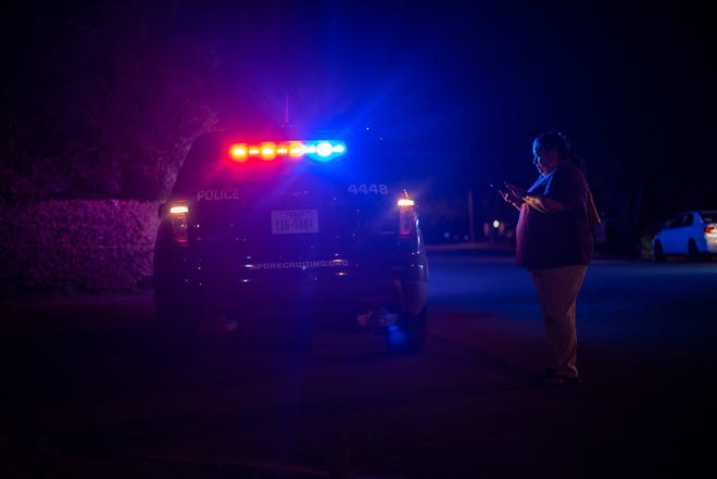 Veronica Martinez stands near a police car that is blocking Shadywood Drive on Friday night in South Austin after an officer-involved shooting. [Sergio Flores For AMERICAN-STATESMAN]