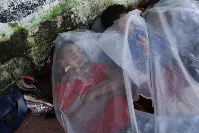 Central American migrants traveling with a caravan to the U.S., use a piece of plastic as covering as they sleep on a sidewalk in Huixtla, Mexico, Tuesday, Oct. 23, 2018. The caravan, estimated to include more than 7,000 people, had advanced but still faced more than 1,000 miles, and likely much further, to the end of the journey. (AP Photo/Moises Castillo)