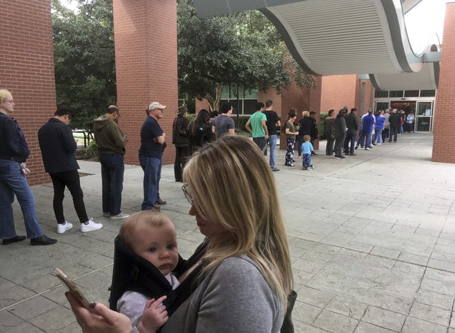 Megan Heckel of Plano holds her daughter Lily as they wait in line for early voting outside Maribelle M. Davis Library in Plano on Monday. Some Texas voters are complaining that while casting Democratic or Republican straight-ticket ballots, voting machines used in 80-plus counties changed their selections to the other party for key races, including the Senate contest between Ted Cruz and Beto O'Rourke. The Secretary of State's office says the problem is occurring on Hart eSlate machines, when voters submit ballots before their choice is fully rendered. It says the machines aren't malfunctioning and instead blames user error. [AP Photo/David Koenig, File]