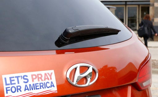 With a "Let's Pray For America" bumper sticker in the foreground, on Thursday, Oct. 25, 2018, a woman walks into a mall in Bloomingdale, Ill. that's housing a polling place for early voters. As Americans head to the polls for this midterm election, they are very polarized by issues from immigration and Supreme Court nominees to gun control. (AP Photo/Martha Irvine)