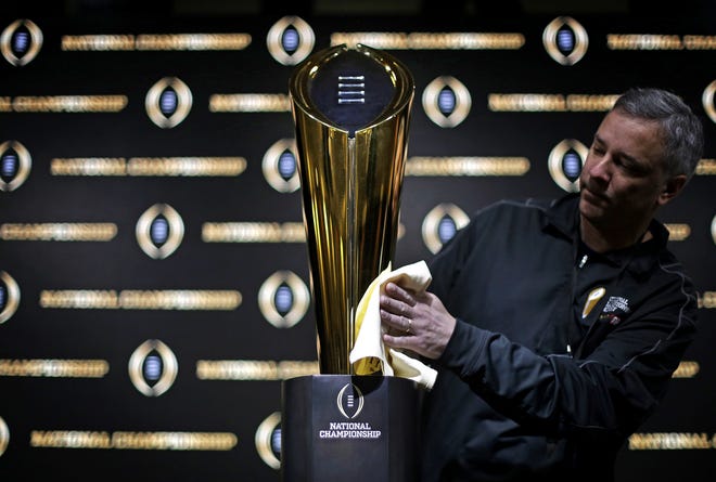 Charley Green buffs the NCAA college football championship trophy before a coaches news conference on Jan. 7 in Atlanta. [AP Photo/David Goldman, file]