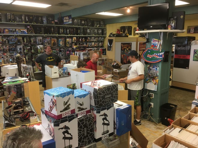 Rick Whitelock, right, talks with customers in the midst of his shop, New Force Comics, where boxes are stacked and carpet has been removed in the wake of Hurricane Michael damage. [TONY SIMMONS/THE NEWS HERALD]