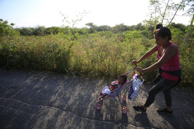 A woman pushes her daughter in a stroller as a thousands-strong caravan of Central Americans hoping to reach the U.S. border moves onward from Juchitan, Oaxaca state, Mexico, Thursday, Nov. 1, 2018. Thousands of migrants resumed their slow trek through southern Mexico on Thursday, after attempts to obtain bus transport to Mexico City failed. (AP Photo/Rebecca Blackwell)