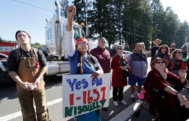 FILE - In this Oct. 17, 2018, file photo, a supporter of Initiative 1631 holds a sign referencing the Nisqually Indian Tribe during a rally supporting I-1631, a November ballot measure in Washington state that would charge a fee on carbon emissions from fossil fuels. Money has poured into the state for the campaign against I-1631, mostly from oil companies. (AP Photo/Ted S. Warren, File)