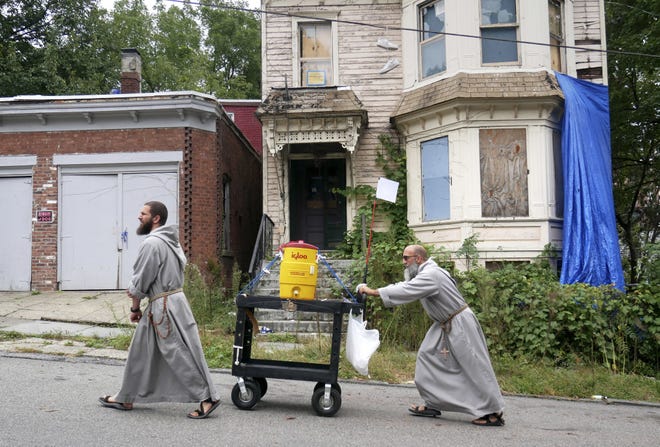 Rev. Giuseppe Siniscalchi, right, and Brother Peter Anthony Curtis push a cart with cold drinks through the streets of Newburgh, N.Y. The brothers use the cart, usually filled with drinks or snacks, as a way to strike up conversations with people. [Seth Wenig/AP Photo]