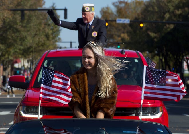 A gust of wind whips American flags and the hair of AMVETS Post 13 queen Kayce Revelle as Post 13 Commander Danny Brewer waves to spectators during the 2018 Veterans Day Parade in Lexington on Saturday morning. [Donnie Roberts/The Dispatch]