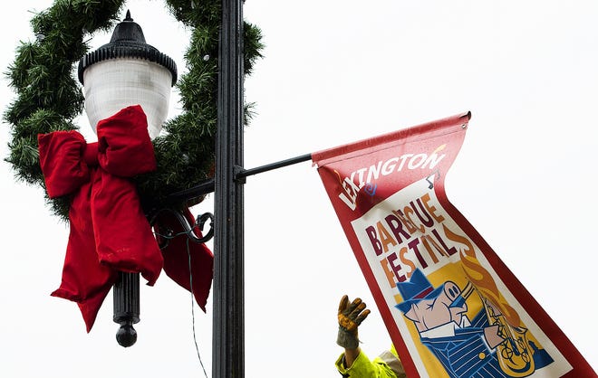 The Christmas season begins as an ElectriCities worker removes a Barbecue Festival banner after installing a wreath on a lamp post on the Square on Tuesday morning. [Donnie Roberts/The Dispatch]