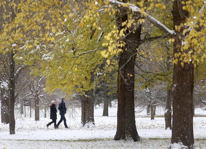 An autumn snow fell in Madison, Wis., on Friday, where Jennyffer Cruz and Duncan Sutherland walked the grounds of the University of Wisconsin Arboretum. [John Hart/Wisconsin State Journal via AP]