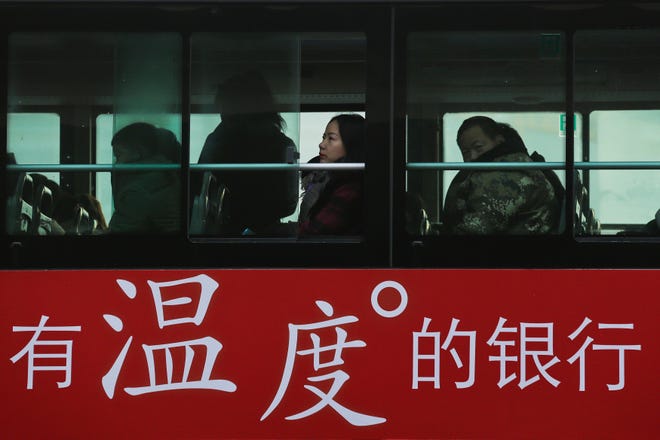 Commuters look out of a window of a bus with a bank advertise during the morning rush hour in Beijing, Tuesday, Nov. 13, 2018. The potential damage to global trade brought on by President Donald Trump's tariffs battle with Beijing is looming as leaders of Southeast Asian nations, China, the U.S. and other regional economies meet in Singapore this week. The advertisement reads "A warm-hearted bank." (AP Photo/Andy Wong)