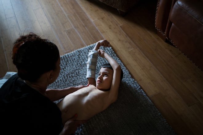 Jourdan stretches his arms with his mother, Chelsi, as part of his daily physical therapy. [Photo for The Washington Post by Annie Flanagan]