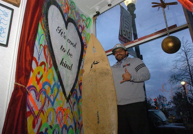 Gnome Surf founder Chris Antao with the painting It's Cool to be Kind, that inspired the name of the calendar. [Herald News photo | Dave Souza]