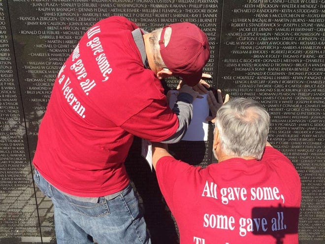 Pontiac resident Jack Groves, left, traces the names of his fallen comrades at the Vietnam Memorial Wall while his brother, John Groves, holds the paper in place.