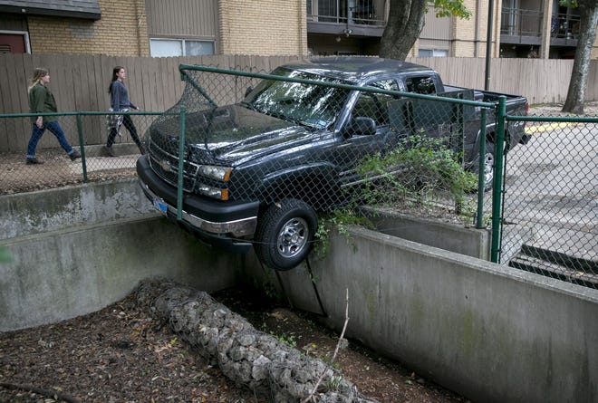 Women walk past a pickup truck that crashed through a fence and got stuck in a retention pond in the parking lot of the Austin American-Statesman next to the Ann and Roy Butler Hike-and-Bike Trail on Monday November 19, 2018.  A witness said the driver left the scene.  [JAY JANNER/AMERICAN-STATESMAN]