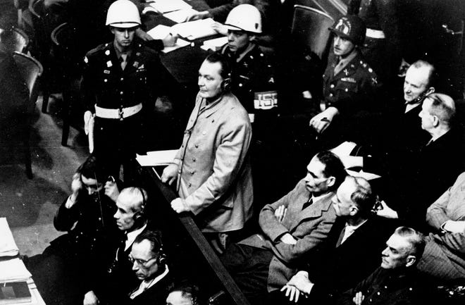Reichsmarshal Hermann Goering stands in the prisoner's dock at the Nuremberg War Crimes Trial on Nov. 21, 1945, in Germany. He is entering a plea of not guilty to the International Military Tribunal Indictment. Goering is wearing headphones of the court translating system. [The Associated Press]