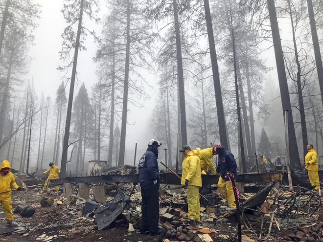After a brief delay to let a downpour pass, volunteers resume their search for human remains at a mobile home park in Paradise, Calif., on Friday. [AP Photo/Kathleen Ronayne]