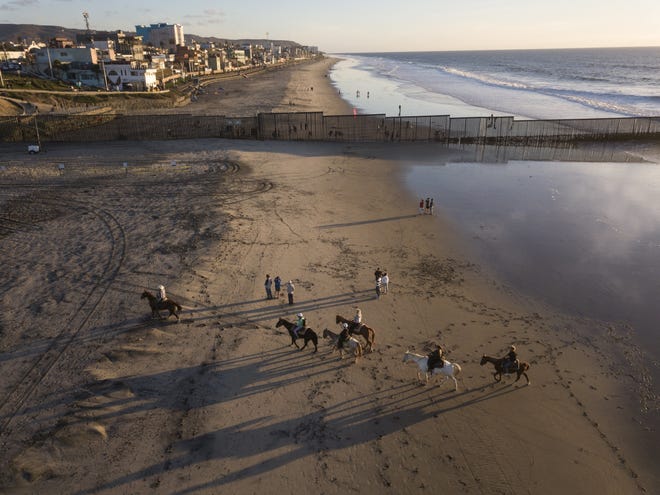People ride horses near the U.S.-Mexico border structure in San Diego, Friday, Nov. 23, 2018. The mayor of Tijuana has declared a humanitarian crisis in his border city and says that he has asked the United Nations for aid to deal with the approximately 5,000 Central American migrants who have arrived in the city. (AP Photo/Rodrigo Abd)