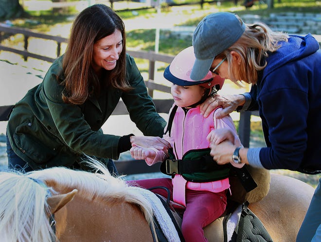 Delane Clark, left, a physical therapist at Shining Hope Farms, along with fellow physical therapist Leslie Weatherhead, right, get Emma ready for her horseback ride at the farm. [JOHN CLARK/THE GASTON GAZETTE]