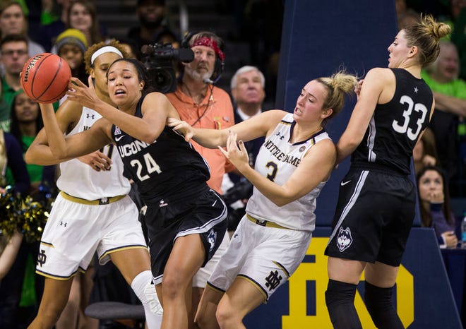 Connecticut's Napheesa Collier passes the ball away after coming down with a rebound between Notre Dame's Brianna Turner, left, and Marina Mabrey on Sunday in South Bend, Indiana. [ASSOCIATED PRESS]