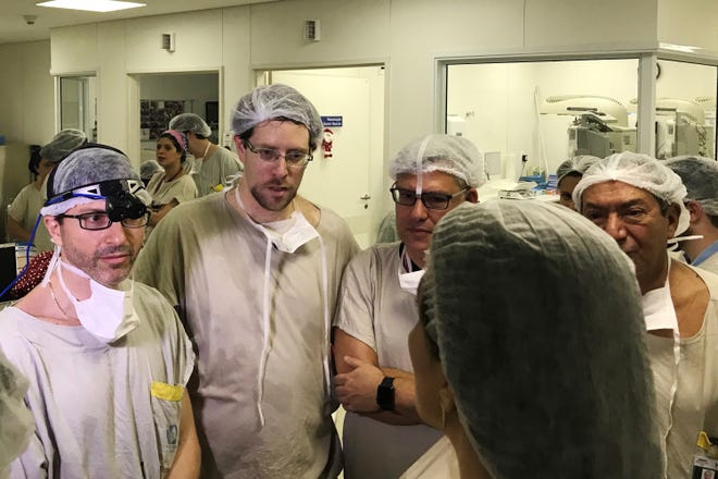 In this Dec. 15, 2017 photo provided by transplant surgeon Dr. Wellington Andraus, left with magnifying glasses, he and Dr. Dani Ejzenberg, second left, confer with colleagues at the Hospital das Clinicas of the University of Sao Paulo School of Medicine, Sao Paulo, Brazil, on the day of the birth of the baby girl born to a woman with a uterus transplanted from a deceased donor. Nearly a year later, mother and baby are both healthy. (Courtesy Dr. Wellington Andraus via AP)