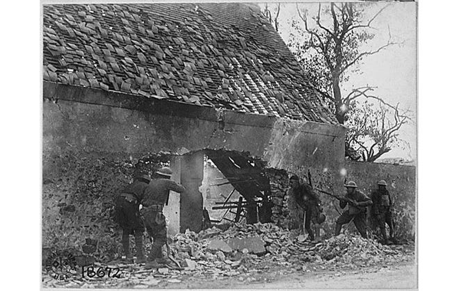 This photo, which is part of an exhibit on display at the Topeka and Shawnee County Public Library, shows American infantrymen peering through a large hole in the concrete side of a building as they do battle with the Germans in July 1918 on the outer edge of a town in France. [National Archives]