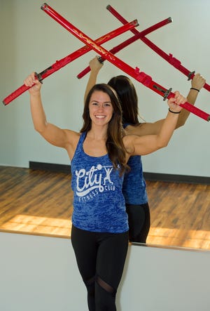 City Fitness personal trainer and competitive body builder Makala Watkins holds two swords she won in a recent bodybuilding competition. [Donnie Roberts/The Dispatch]