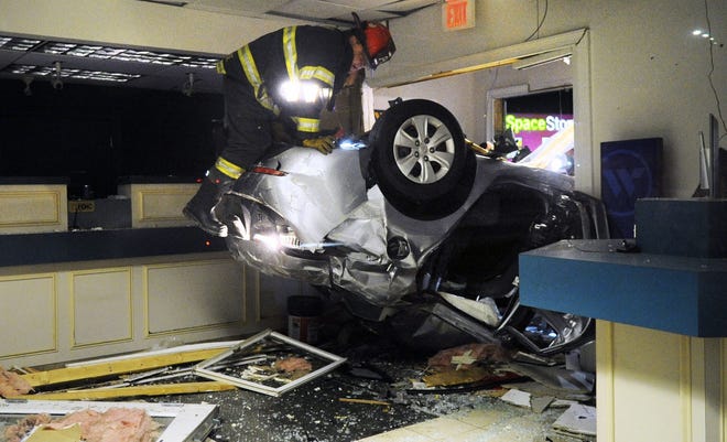 A firefighter climbs over a car that crashed through a wall and landed inside a Webster Bank branch in Brockton early Friday. The driver was flown to a Boston hospital with serious injuries.  [Marc Vasconcellos/The Enterprise]