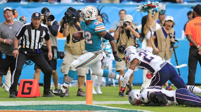 Miami Dolphins running back Kenyan Drake (32) scores on the final play of the game to defeat the New England Patriots at Hard Rock Stadium in Miami Gardens on Sunday. The Dolphins won 34-33. [Al Diaz / Miami Herald via AP]