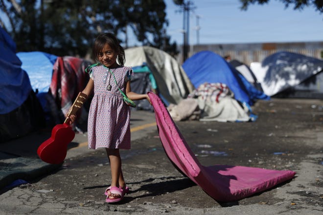 Samira Lopez, 5, of Honduras carries a wet mattress and a guitar as she plays in a migrant camp where a few hundred Central Americans continue to camp out outside the closed Benito Juarez sports complex, in Tijuana, Mexico, Saturday, Dec. 8, 2018. Spurred by complaints from local residents, authorities are increasing pressure on migrants living outside the former shelter adjacent to the U.S. border to move to the more distant Barretal shelter, where more than 2,000 others who arrived with caravans are now camping. (AP Photo/Rebecca Blackwell)