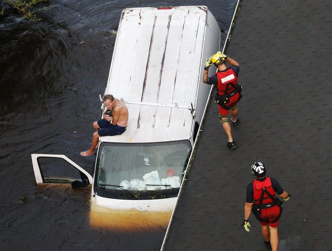 U.S. Coast Guard rescue swimmers Samuel Knoeppel, center, and Randy Haba, bottom right, approach Willie Schubert on a stranded van in Pollocksville, N.C., on Sept. 17, 2018, in the aftermath of Hurricane Florence. (AP Photo/Steve Helber)