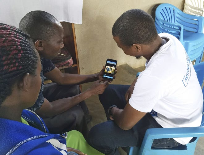Timothy Bandirana, holding the phone, with Samuel Asiimwe, right, and Joy Asiimwe, left, work on translating a story from the Bwisi language in western Uganda, guided by the Story Producer app. Cedarville University students helped create the app, which was field-tested in Kenya and Uganda during the summer. [Robin Rempel]