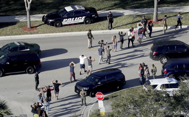 FILE - In this Feb. 14, 2018 file photo, students hold their hands in the air as they are evacuated by police from Marjory Stoneman Douglas High School in Parkland, Fla., after a shooter opened fire on the campus. The police response to the Florida high school massacre was delayed because school officials rewound a school surveillance video, making officers think the gunman was still in the building, the South Florida Sun-Sentinel reports. (Mike Stocker/South Florida Sun-Sentinel via AP, File)