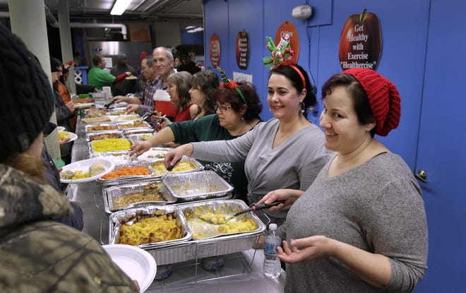 Sarah Brenneman, front, and Tara DiFonzo are all smiles as they greet guests at the second annual Christmas Eve Dinner for the Homeless, held at the Boys and Girls Club on Kendrick Avenue in Woonsocket. [The Providence Journal / Kris Craig]