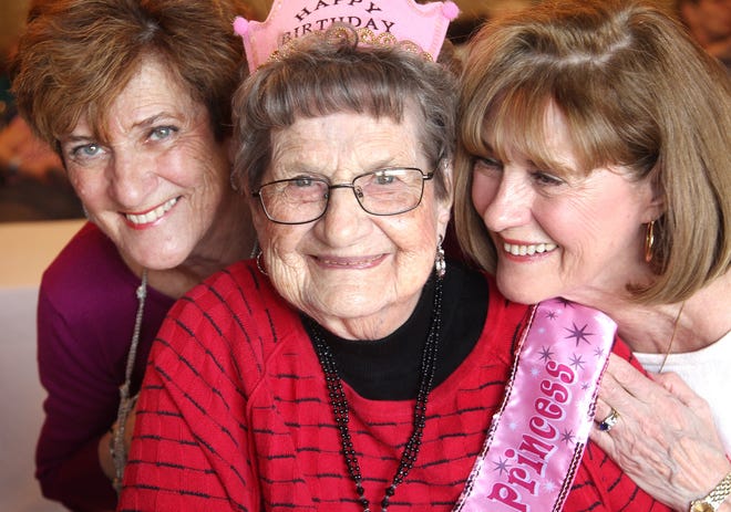 Catherine Thibodeau of Weymouth and Mary Cosgrove of Hingham help their mother, Margaret AuCoin, celebrate her 107th birthday at Colonial Rehabilitation Nursing home in Weymouth on March 27, 2018. (Gary Higgins/The Patriot Ledger)