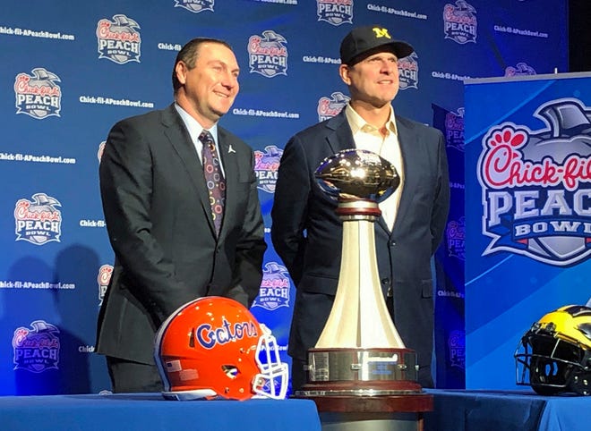 Florida coach Dan Mullen and Michigan coach Jim Harbaugh stand alongside the George P. Crumbley Trophy on Friday in Atlanta. The teams play in the Peach Bowl today. [Charles Odum/The Associated Press]