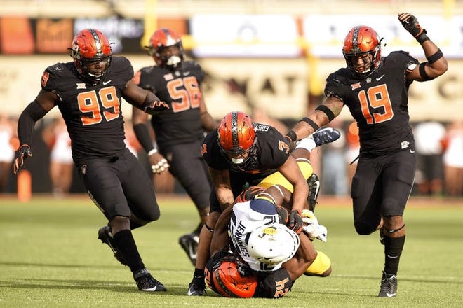 Oklahoma State defensive tackle Trey Carter (99) and offensive lineman Larry Williams (56) watch as teammates Kenneth Edison-McGruder (3), linebacker Justin Phillips (19) and safety Jarrick Bernard (24) stop the advance of West Virginia wide receiver Gary Jennings Jr. during the first half of an NCAA college football game in Stillwater, Okla., on Saturday, Nov. 17. Oklahoma State upset West Virginia 45-41. [Brody Schmidt/The Associated Press]