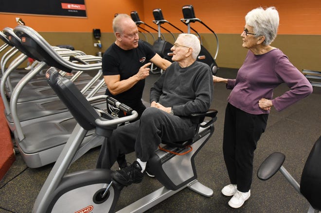 Shep Bryan, 96, works out on a recumbent bike under the instruction of fitness coach Stan Gorman, as his wife, Mary Ann Bryan, watches at a Bailey's Gym in Jacksonville. [Bob Self/Florida Times-Union]
