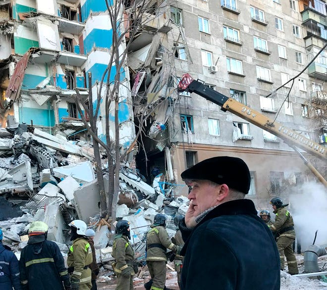 In this photo provided by Chelyabinsk Region Governor Press Service, Governor of the Chelyabinsk Region Boris Dubrovsky, center, speaks on the phone as Emergency Situations employees work at the scene of a collapsed apartment building, in Magnitogorsk, a city of 400,000 about 1,400 kilometers (870 miles) southeast of Moscow, Russia, Monday, Dec. 31, 2018. Russian emergency officials say that at least four people have died after sections of an apartment building collapsed after an apparent gas explosion in the Ural Mountains region. (Chelyabinsk Region Governor Press Service photo via AP)