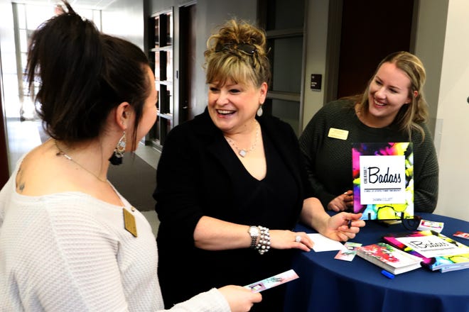 Author and artist Shawna Coate Elliott, center, signs bookmarks for Ann Marie, left, and Christa Jumper on Tuesday, Jan. 15, 2019, during an artist's reception and book signing in the Smith-Pendergraft Campus Center on the University of Arkansas at Fort Smith campus. Several large pieces from Elliot's "Be A Creative Badass: 52 Whole-Life Activities to Boost Your Creativity," exhibit will be on display in the campus center through March 1 and will be open to the public for free. [JAMIE MITCHELL/TIMES RECORD]