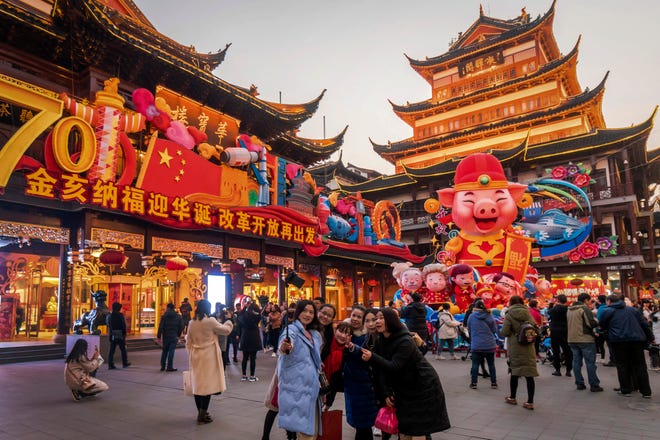 In this Jan. 17, 2019, photo, women take a selfie as others tour at the Yu Garden decorated with pig statues for Lunar New Year in Shanghai. China’s 2018 economic growth fell to a three-decade low as activity cooled amid a tariff war with Washington. (Chinatopix via AP)