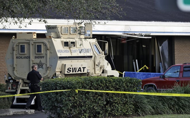 A Sebring, Fla., police officer stands near a Highlands County Sheriff's SWAT vehicle that is stationed in front of a SunTrust Bank branch, Wednesday, in Sebring, where authorities say five people were shot and killed. [Chris O'Meara/AP Photo]