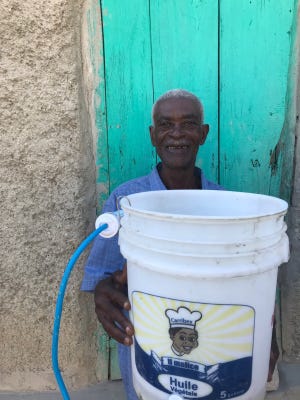 A man holds five-gallon drum with a folter attached. The system providess clean, drinkable water to a small family.