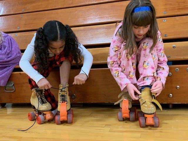 Carroll Catholic second grade students Amaya Stewart, left, and Grace Nutter, right, lace up their skates with the goal of getting to skate around the gym with fellow classmates. [Photo by Jean Ann Miller/The Courier]