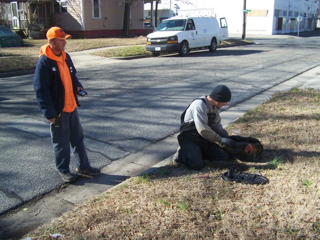 Tim Stephens, meter technician for the City of Kinston, left, watches Anthony Micklash of Vanguard Utilities install a new smart meter on E. Lenoir Street. [Photo by Eddie Fitzgerald]