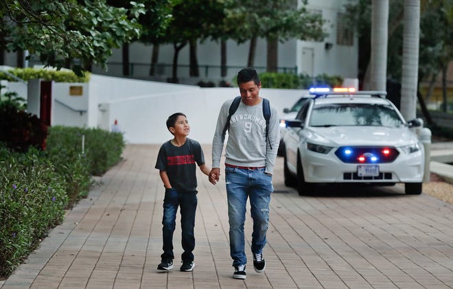 Mynor Diaz-Berduo, 29, of Guatemala, walks down a path with his 10 year-old son (name withheld) outside of the immigration courthouse after court hearings were canceled on Thursday, Jan. 31, 2019, in Miami. U.S. immigration officials blame the government shutdown and the extreme winter weather for confusion about immigration court hearings. In an emailed statement, the part of the Justice Department overseeing immigration courts said some immigrants with notices to appear Thursday wouldn't be able to proceed with those hearings. (AP Photo/Brynn Anderson)