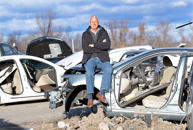 Paul Kawolis, owner of Linder's Used Auto Parts in Worcester, sits atop a totally wrecked car in the company's auto graveyard. [T&G Staff/Steve Lanava]