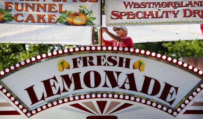 Angel Sanchez hangs a sign on the top of a concession stand Aug. 9 during final preparations for the 2018 Iowa State Fair in Des Moines. The Iowa State Fair said it will require all food and drink vendors to accept credit and debit card payments beginning in 2020. [Charlie Neibergall/The Associated Press]