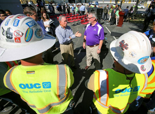 Former New York mayor Michael Bloomberg, left, talks with Orlando Mayor Buddy Dyer during his visit to Orlando Utilities Commission's sustainable energy facility, Friday, Feb. 8, 2018. Bloomberg said Friday that he'll decide by the end of the month whether to seek the presidency. (Joe Burbank/Orlando Sentinel via AP)