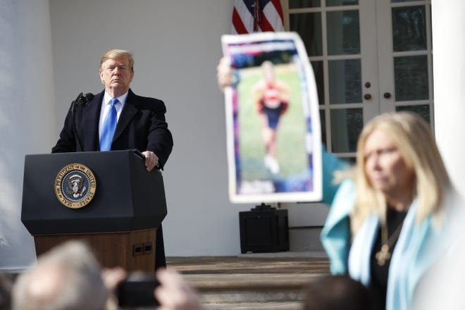 President Donald Trump looks on as an Angel Mom holds up a poster of her daughter, during an event in the Rose Garden at the White House to declare a national emergency in order to build a wall along the southern border, Friday. [PABLO MARTINEZ MONSIVAIS/THE ASSOCIATED PRESS]