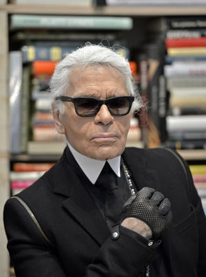 In this Feb. 14, 2014, file photo, Karl Lagerfeld poses for photographers in front of his books prior to the start of an exhibition at the museum Folkwang in Essen, Germany. Chanel's iconic couturier, Karl Lagerfeld, whose accomplished designs as well as trademark white ponytail, high starched collars and dark enigmatic glasses dominated high fashion for the last 50 years, has died. He was around 85 years old. [MARTIN MEISSNER/AP FILE PHOTO]